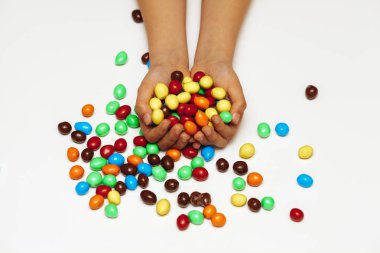 Beyaz arka planda kadınların elleri yuvarlak renkli çikolatalara sarılır.