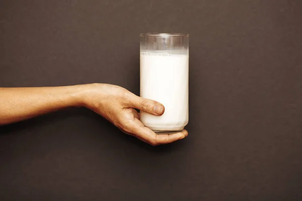 A woman's hand holds a glass of milk on a dark background