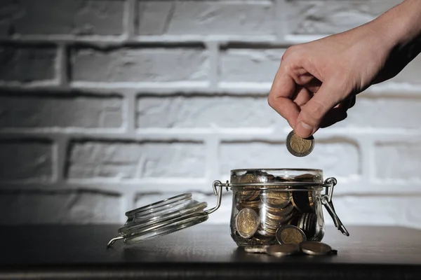 a man\'s hand puts a coin in the jar