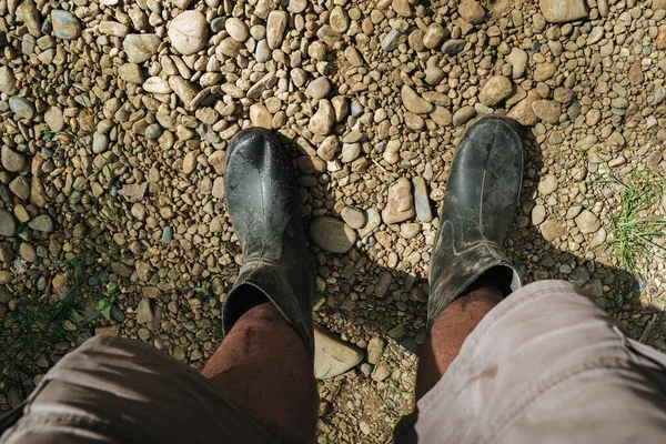 men's feet in muddy rubber boots standing on rocks