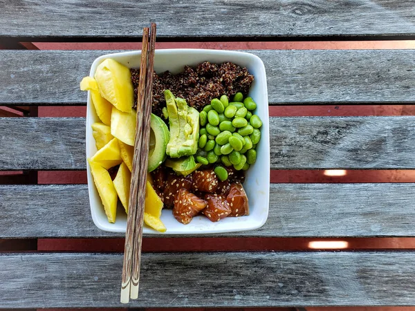 Salmon poke bowl with white rice and red quinoa mango avocado edamame and chopsticks