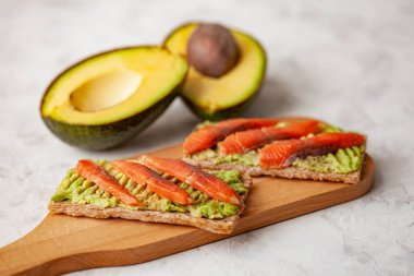 Kırmızı balıklı iki sandviç ve ahşap kesim tahtasında avokado.