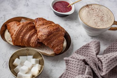 Gri bir masada iki ay çöreği ve kapuçino ile kahvaltı.