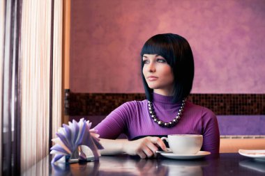 Kafede bir fincan kahveyle oturan genç ve çekici bir kadın.