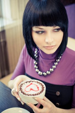 Kafede bir fincan kahveyle oturan genç ve çekici bir kadın.