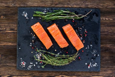 Kara tahtada kekik, biberiye, biber ve tuz taneleriyle üç somon bifteği.