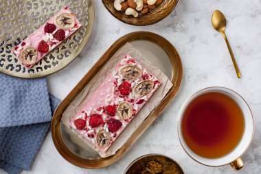 Muz, ahududu ve puf pirinçli el yapımı pembe çikolata bir fincan çayın yanında duruyordu.