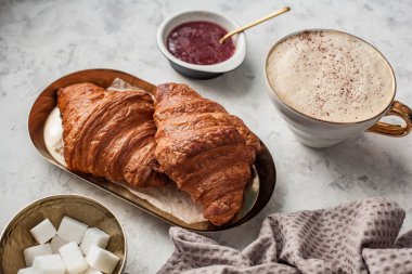 Gri bir masada iki ay çöreği ve kapuçino ile kahvaltı.
