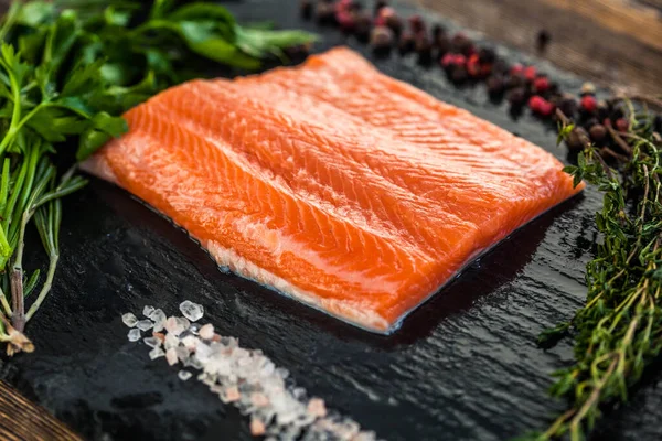 Büyük bir somon bifteği, yeşillik, biber ve karatahtanın üzerinde tuz taneleri.