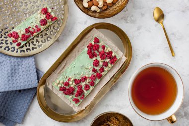 El yapımı yeşil çikolata, ahududu, sedir fıstığı ve kenevir tohumu bir fincan çayın yanında duruyor.