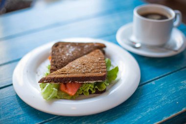Çavdar ekmekli sandviç, kırmızı balık, marul ve bir fincan kahve.