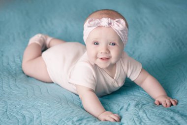 Saç bandı takmış yeni doğmuş bir kız mavi bir battaniyenin üzerinde yatıyor ve gülümsüyor.