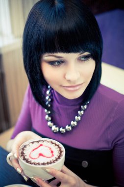 Kafede bir fincan kahveyle oturan genç ve çekici bir kadın.