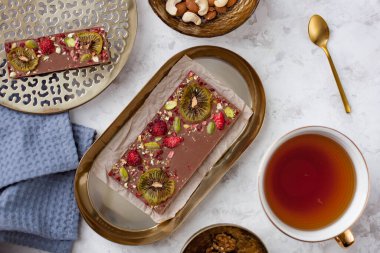 Bir fincan çayın yanında duran el yapımı çikolatalı kivi, çilek ve fındıklı çikolata.