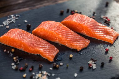 Kara tahtada kekik, biberiye, biber ve tuz taneleriyle üç somon bifteği.