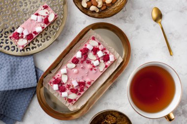 El yapımı pembe çikolata, marşmelov, ahududu ve badem bir fincan çayın yanında duruyor.