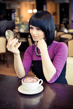 Kafede bir fincan kahveyle oturan genç ve çekici bir kadın.