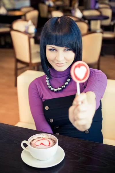 Kafede bir fincan kahve ve lolipopla genç bir kadın.