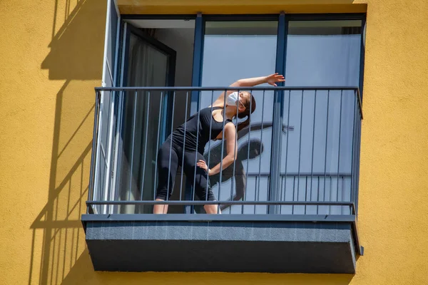 Maskeli kadın dairenin balkonunda yoga yapıyor. Evde kal.