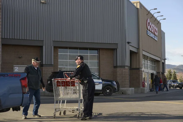 Helena, Montana / ABD - 24 Mart 2020: Gülümseyen bir polis memuru yaşlı bir adamın bakkaldaki eşyalarını boşaltmasına ve alışveriş arabasını geri vermesine yardım ediyor. Coronavirus salgını sırasında ekstra Costco polis güvenliği. 