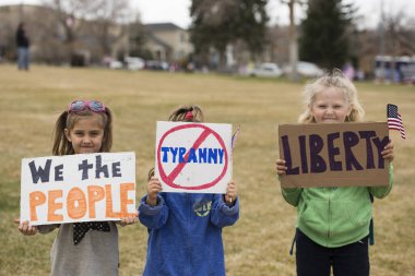 Helena, Montana - April 19, 2020: Children, young girls, holding liberty and tyranny sign at the protest rally at the Capitol due to the government shutdown over Coronavirus Covid-19. clipart