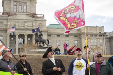Helena, Montana - 19 Nisan 2020: Protestocular, Coronavirus 'un kapanması nedeniyle işi yeniden açmak isteyen Bedford Milis Bayrağı' na bakarak Amerikan bayrakları taşıyorlar..
