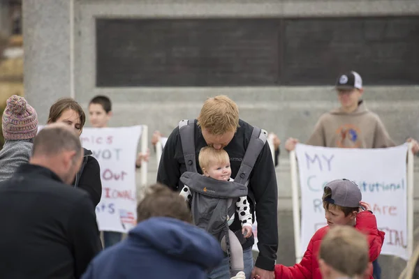 Helena, Montana - 19 Nisan 2020: Erkek ve baba Coronavirus yüzünden evde kalma ve hükümetin kapatılması üzerine düzenlenen bir protestoda bebeğin başını öpüyor.