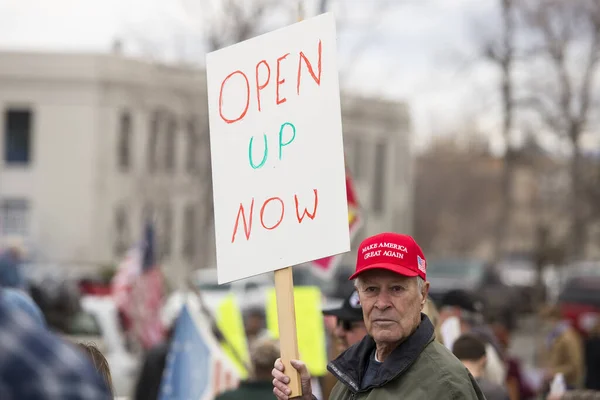 Helena, Montana - 19 Nisan 2020: Protestocu kapatma üzerine bir protesto mitinginde pankart tutuyor ve Coronavirus 'tan korktuğu için evde bekliyor. Amerika 'yı Yeniden Büyük Yap şapkası giyen yaşlı adam.