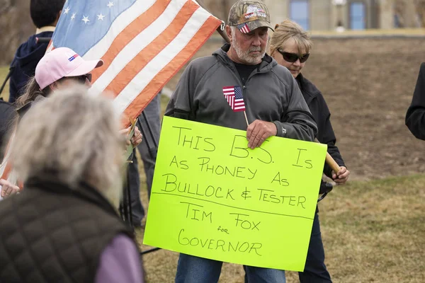Helena, Montana - 19 Nisan 2020: Bir gösterici hükümet kapatma eylemi sırasında validen nefret eden bir neon ışığı tutuyor. Trump Train kamuflaj şapkası giyen yaşlı adam..