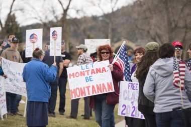 Helena, Montana - 19 Nisan 2020: İşyerlerinin Coronavirus tarafından kapatılması nedeniyle işe dönmek isteyen kızıl saçlı bir kadın. Kongre binasında diğer göstericilerden oluşan bir kalabalıkla protesto.