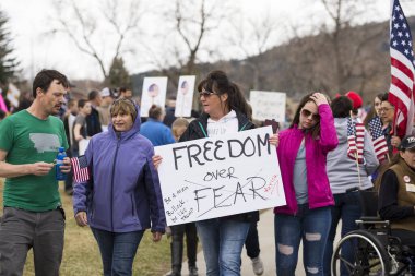 Helena, Montana - April 19, 2020: A woman protesting and holding a freedom over fear sign at a Rally during the Coronavirus government shutdown. A crowd of protestors in the background. clipart