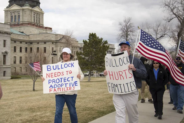 Helena, Montana - 19 Nisan 2020: Bir erkek ve bir kadın, valinin hükümet tarafından Capitol 'de kapatılmasının protesto gösterilerinde evlat edinilen aileleri korumadığını belirten pankartlar taşıyor..