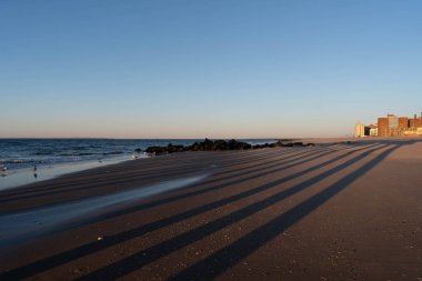 New York City, New York / ABD - 7 Nisan 2020: Brighton sahilinde güneş doğuyor, kızıl gökyüzü, mavi bulutlar ve derin mavi okyanus suyuyla.