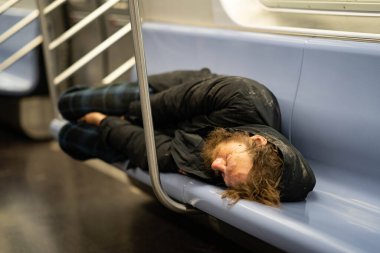New York City, New York / ABD - 6 Nisan 2020: Metro vagonunda uyuyan evsiz bir adam, New York 'ta boş bir New York şehrinde oturan ve Coronavirus salgını sırasında yemek yiyen bir evsiz..