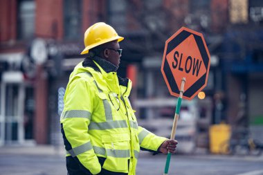 New York, New York - ABD Nisan 12020: Karantina Coronavirus sırasında yolda trafik dursun diye elinde turuncu yavaş işareti tutan sarı Rob giymiş inşaat işçisi.
