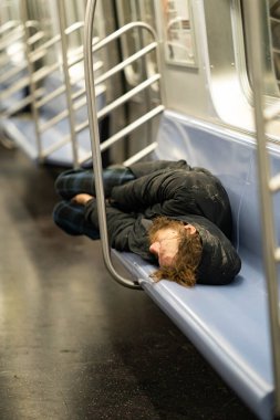 New York City, New York / ABD - 6 Nisan 2020: Metro vagonunda uyuyan evsiz bir adam, New York 'ta boş bir New York şehrinde oturan ve Coronavirus salgını sırasında yemek yiyen bir evsiz..