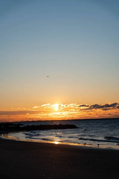 New York City, New York / USA - April 7 2020: Sunrise over the Atlantic Ocean at Brighton beach, with red sky, blue clouds and deep blue ocean water.