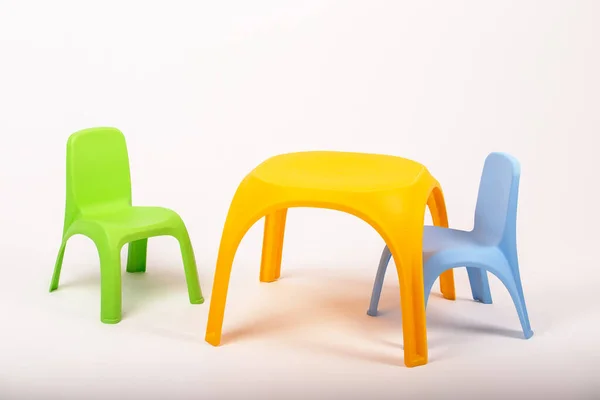 Sarı plastik çocuk masası ve beyaz arka planda iki sandalye.