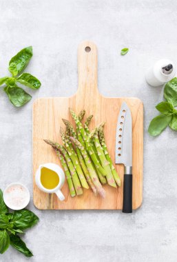 Kuşkonmaz pişirme konsepti, yeni kuşkonmazlarla dolu bir kesme tahtasının tepesinden aşağı bakmak, mutfak masasına uzanmak, sağlıklı yemek pişirme fikri.