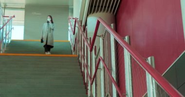 Yüz maskeli kadın tren istasyonunda merdivenlerden iniyor.