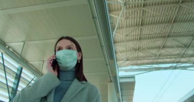Tren istasyonunda maskeli bir kadın telefonla konuşuyor.