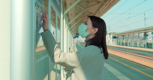 Frau Mit Gesichtsmaske Kontrolliert Fahrplan Bahnhof — Stockvideo