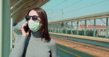 Tren istasyonunda maskeli bir kadın telefonla konuşuyor.