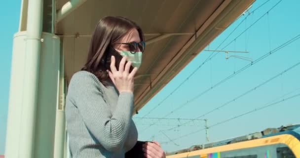 Γυναίκα Μάσκα Προσώπου Μιλάει Στο Τηλέφωνο Στο Σιδηροδρομικό Σταθμό — Αρχείο Βίντεο