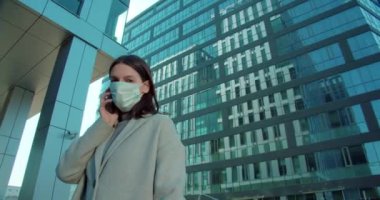 İş bölgesinde yüz maskeli bir kadın telefonla konuşuyor.
