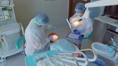 Diş hekimi ve hemşire dişçi muayenehanesindeki hastayı tedavi ediyor.