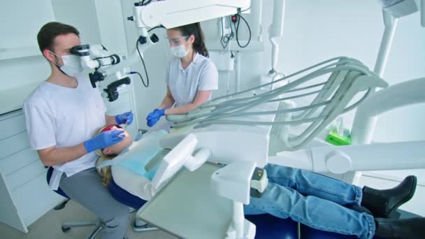 Οδοντίατρος Κοιτάζοντας Μέσα Από Οδοντιατρικό Μικροσκόπιο Κατά Θεραπεία Του Ασθενούς — Αρχείο Βίντεο
