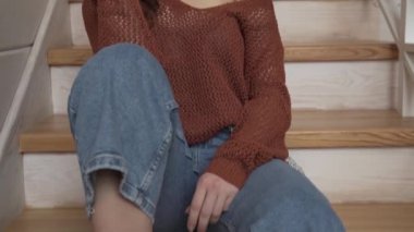 Merdivenlerde oturan kıvırcık saçlı genç kız. Kamera aşağıdan yukarıya hareket eder. Kız gülümsüyor..