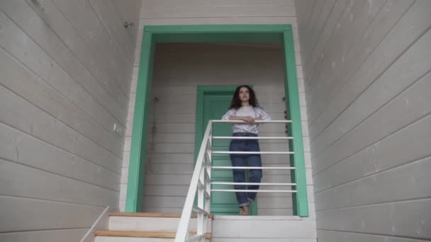 Egy göndör hajú lány áll a második emeleten, közel a lépcsőn, és pózol a kamera az általános terv a keret. — Stock videók