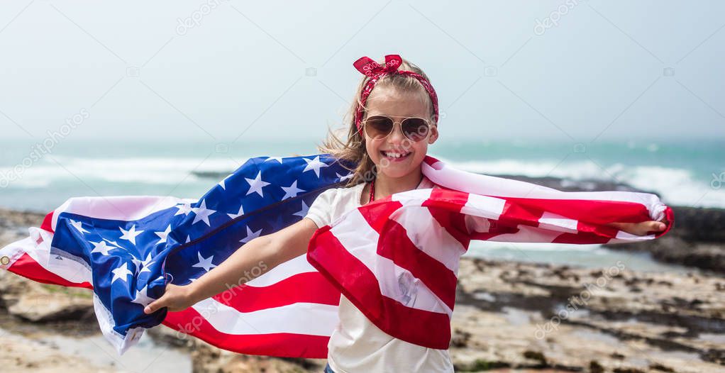 American flag. Little smiling  patriotic girl with long blond hair, red head band  bandana and sunglasses holding an american flag waving in the wind on the ocean beach. National 4 july. Memorial day